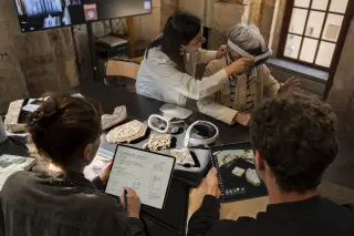 Cultural mediators and a digital developer collaborating around AR devices and historical artifacts in a hybrid heritage space, bathed in warm natural light, with authentic teamwork in progress.