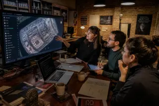Creative team collaborating in a digital studio, illuminated by soft lights and device screens, examining streamed cultural artifact on a large monitor.