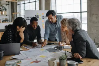 Cultural professionals and entrepreneurs collaborating around a rustic table in a bright, renovated industrial space, focused on planning documents and digital tools