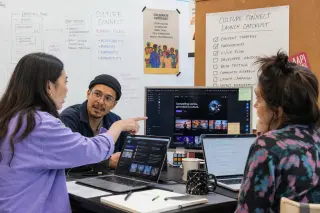 Creative team collaborating in a bright coworking space, reviewing digital mockups and checklists for a cultural streaming platform launch.